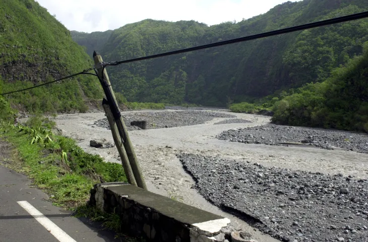 Leaning utility pole beside a washed-out road after a storm